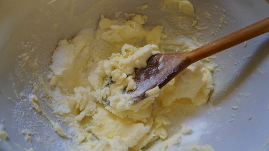 Butter and sugar being mixed with a wooden spoon. 