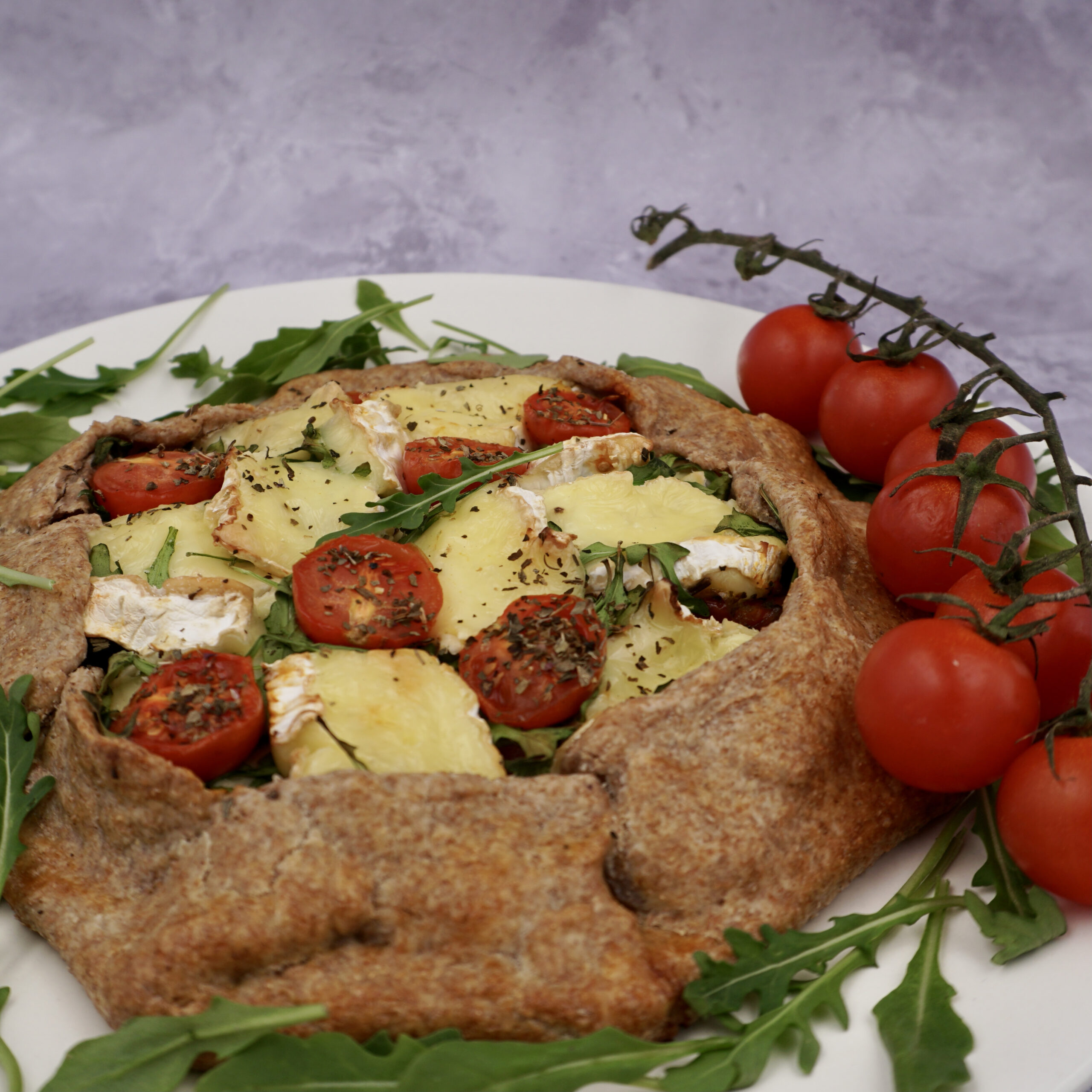 A rustic vegetarian galette on a plate with a stem of cherry tomatoes