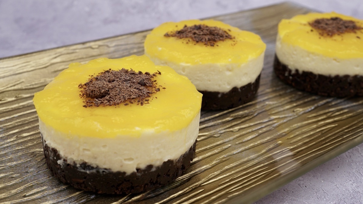 A tray of three individual mango and white chocolate cheesecakes.