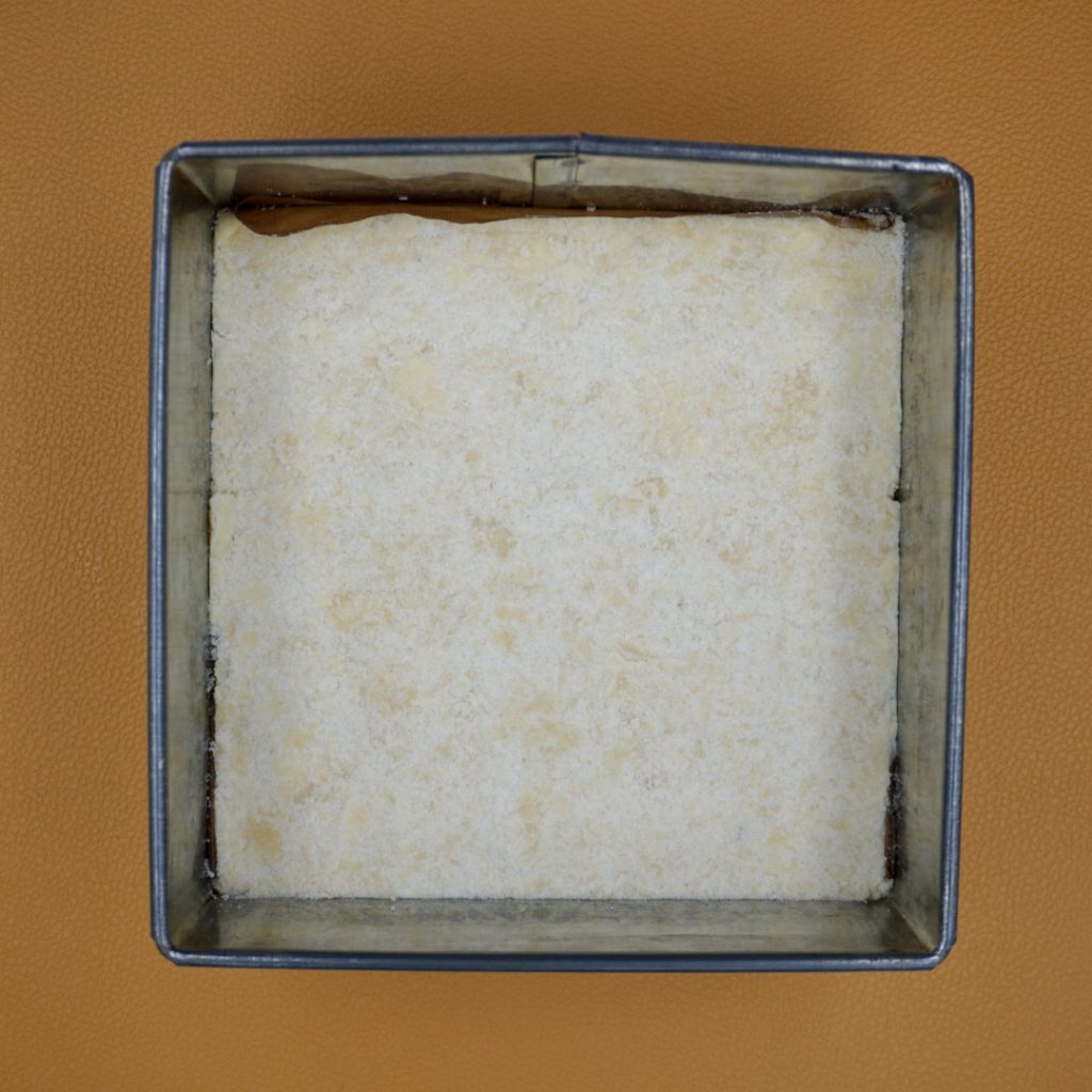 Shortbread mixture in a square cake tin. 