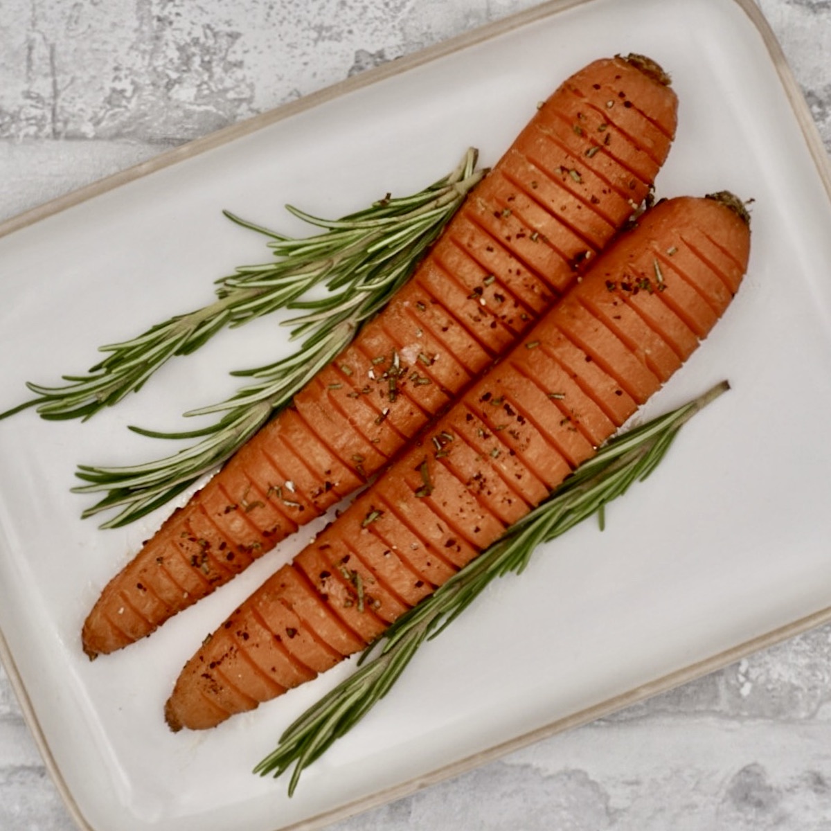 Two hasselback carrots on a serving plate with rosemary garnish