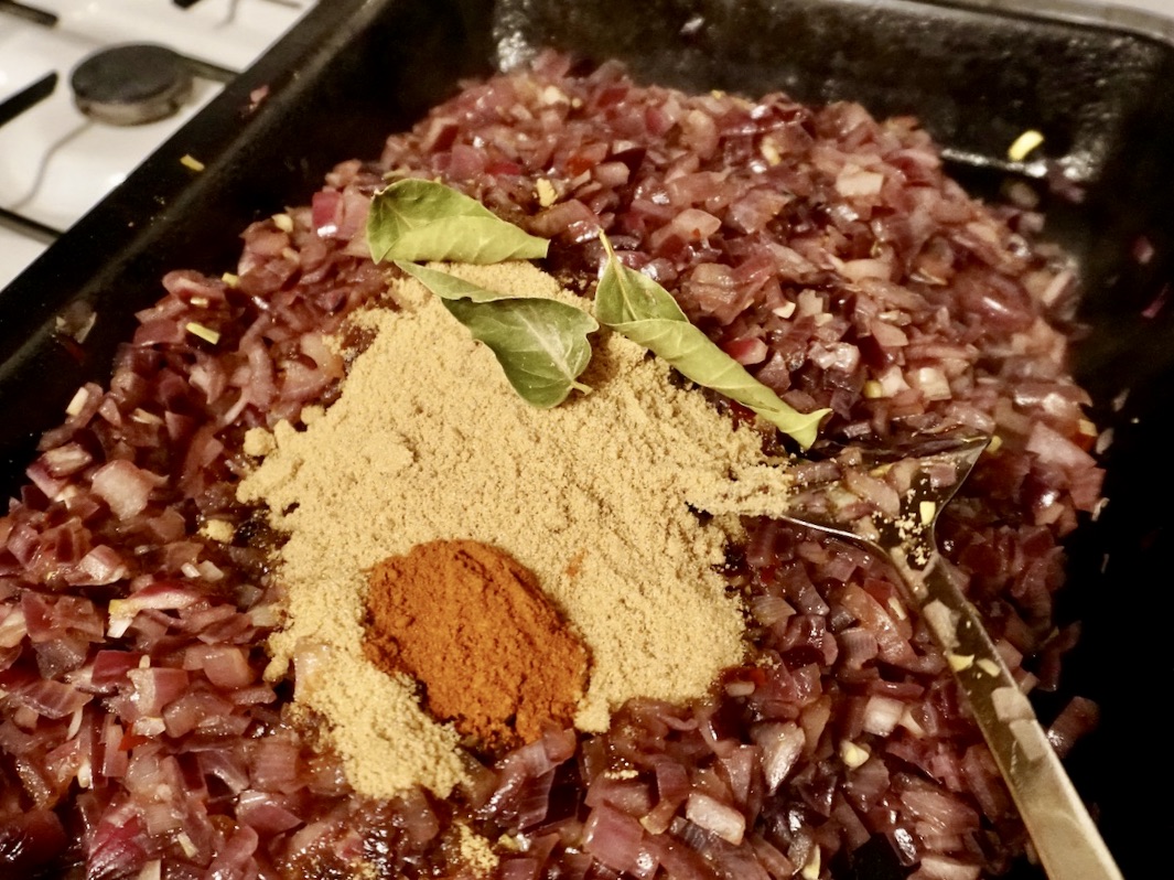 Cooking chopped red onions with spices, sugar and bay leaves. 