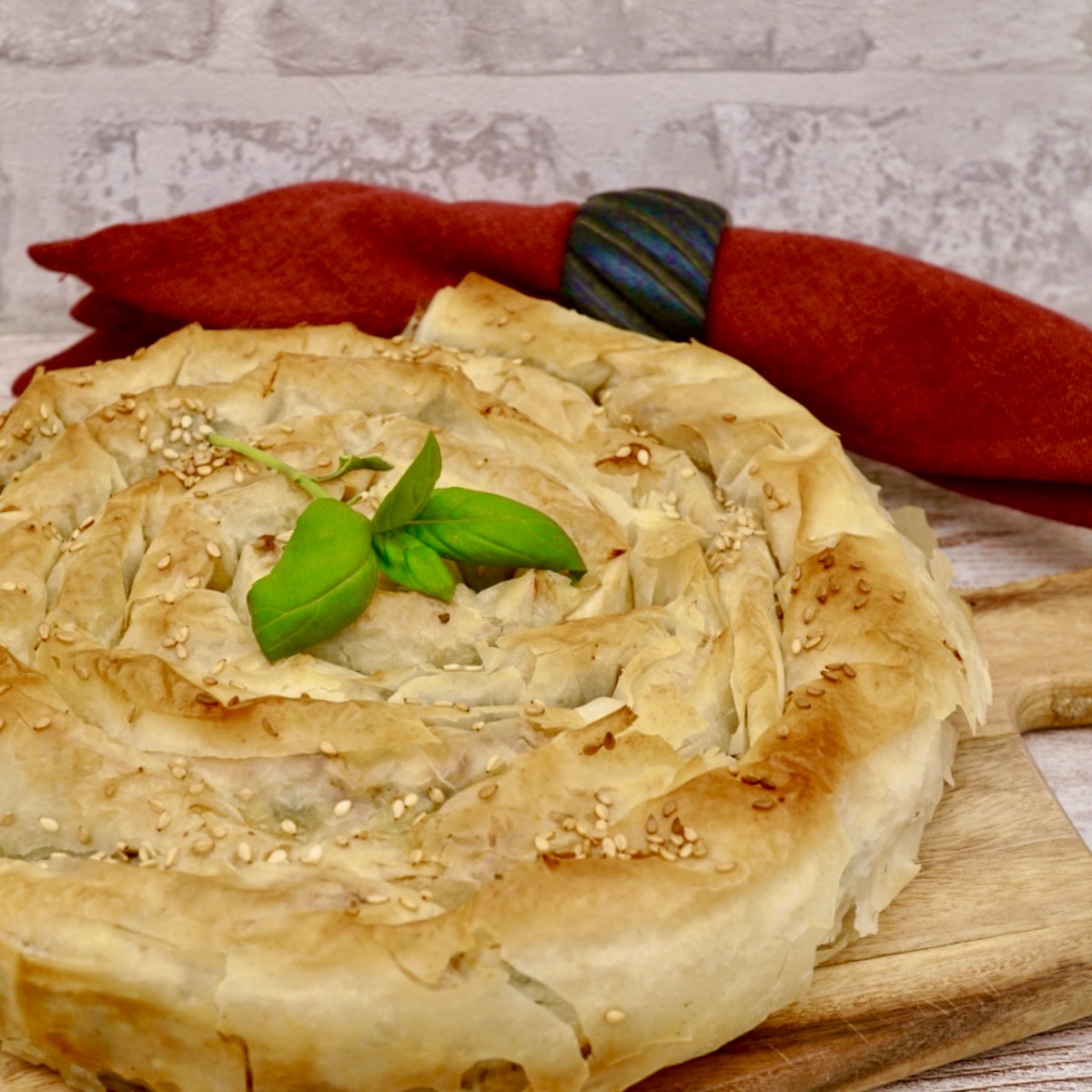 Spanakopita in the form of a spiral on a board, with garnish. 