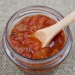 An open jar of red tomato chutney with a spoon.