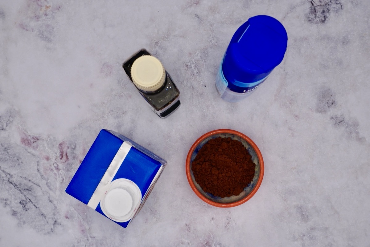 a carton of cream, condensed milk, bottle of vanilla essence an bowl of cocoa powder