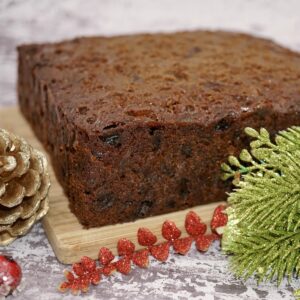 An undecorated square Christmas cake on a board next to Christmas decorations.