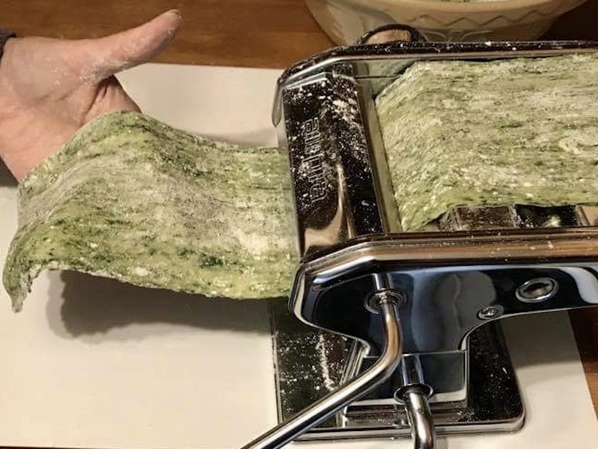 Rolling spinach pasta through a pasta machine