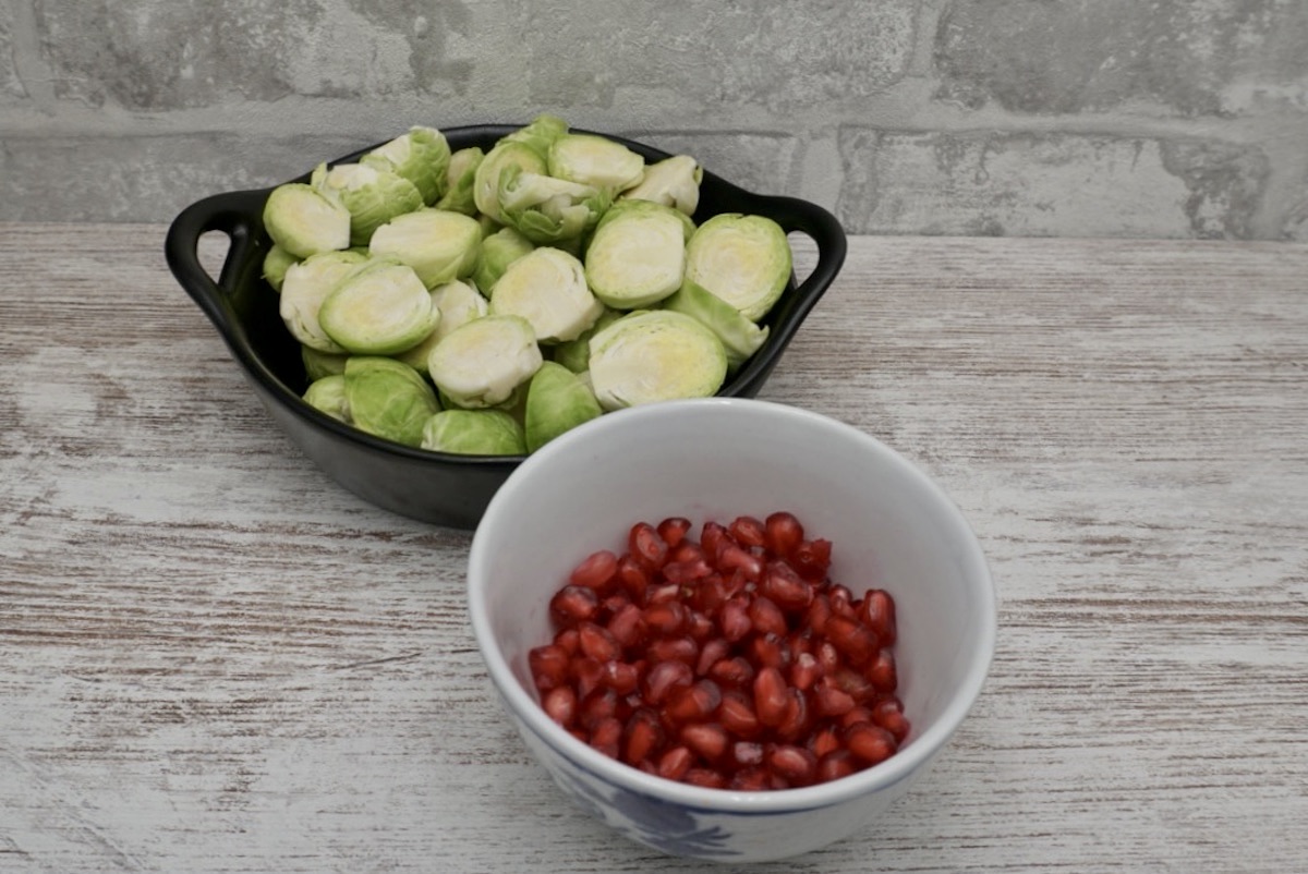 A bowl of sprouts cut in half and a bowl of pomegranate arils 