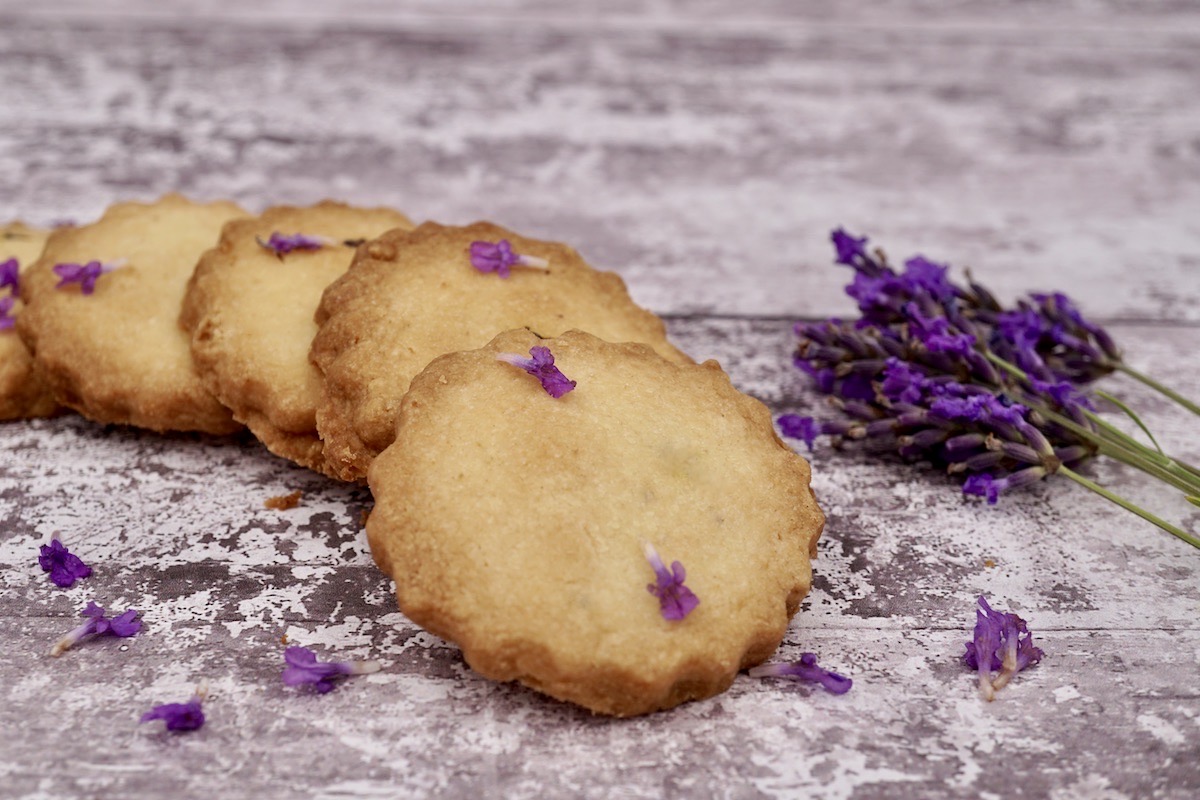 Four lavender shortbread biscuits and some fresh lavender flowers. 