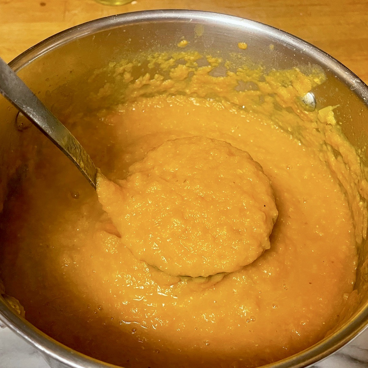 A ladle of spicy carrot and lentil soup in a pan.