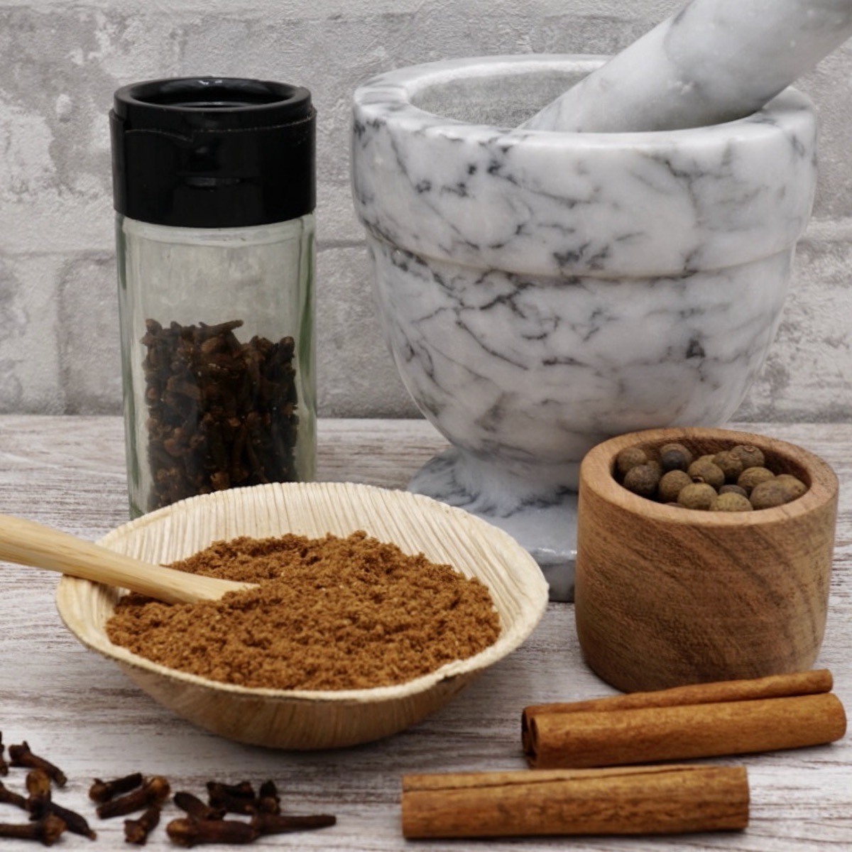 A bowl of mixed spice next to some whole spices and a marble pestle and mortar.