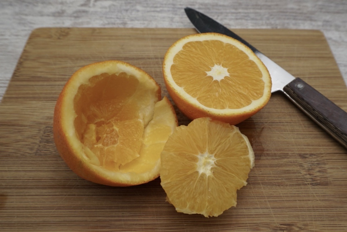 An orange on a chopping board cut in half and half removed from the skin.