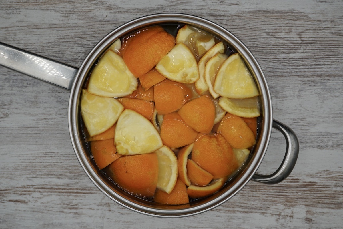 Overhead view of chopped up orange and orange peel in a pan with water.