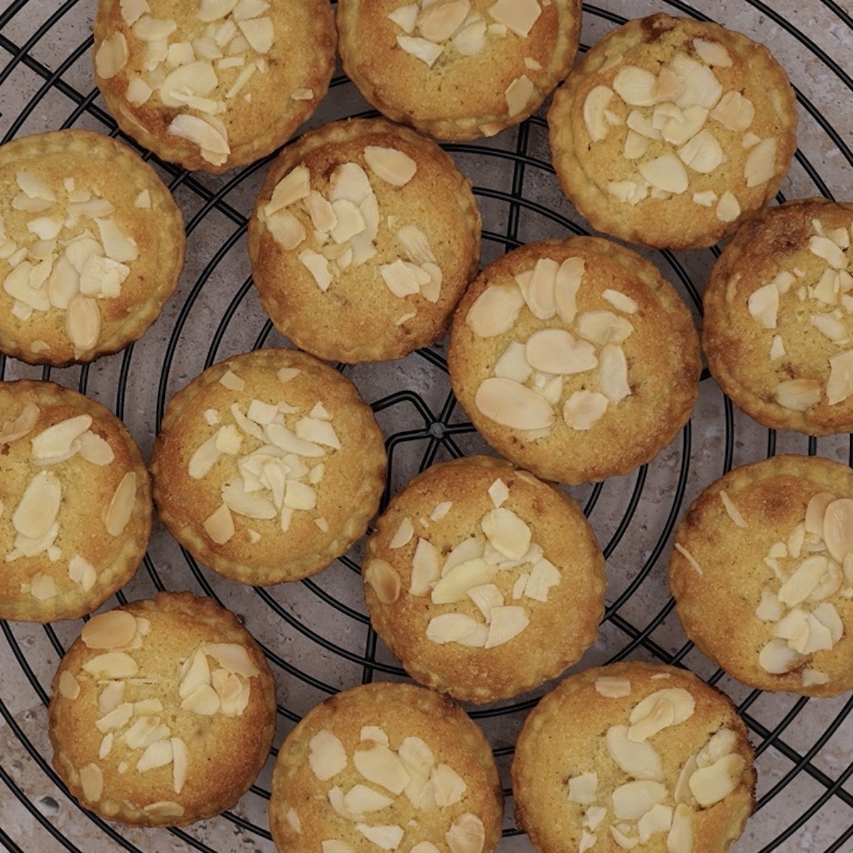 Overhead view of a group of frangipane mince pies on a wire rack.