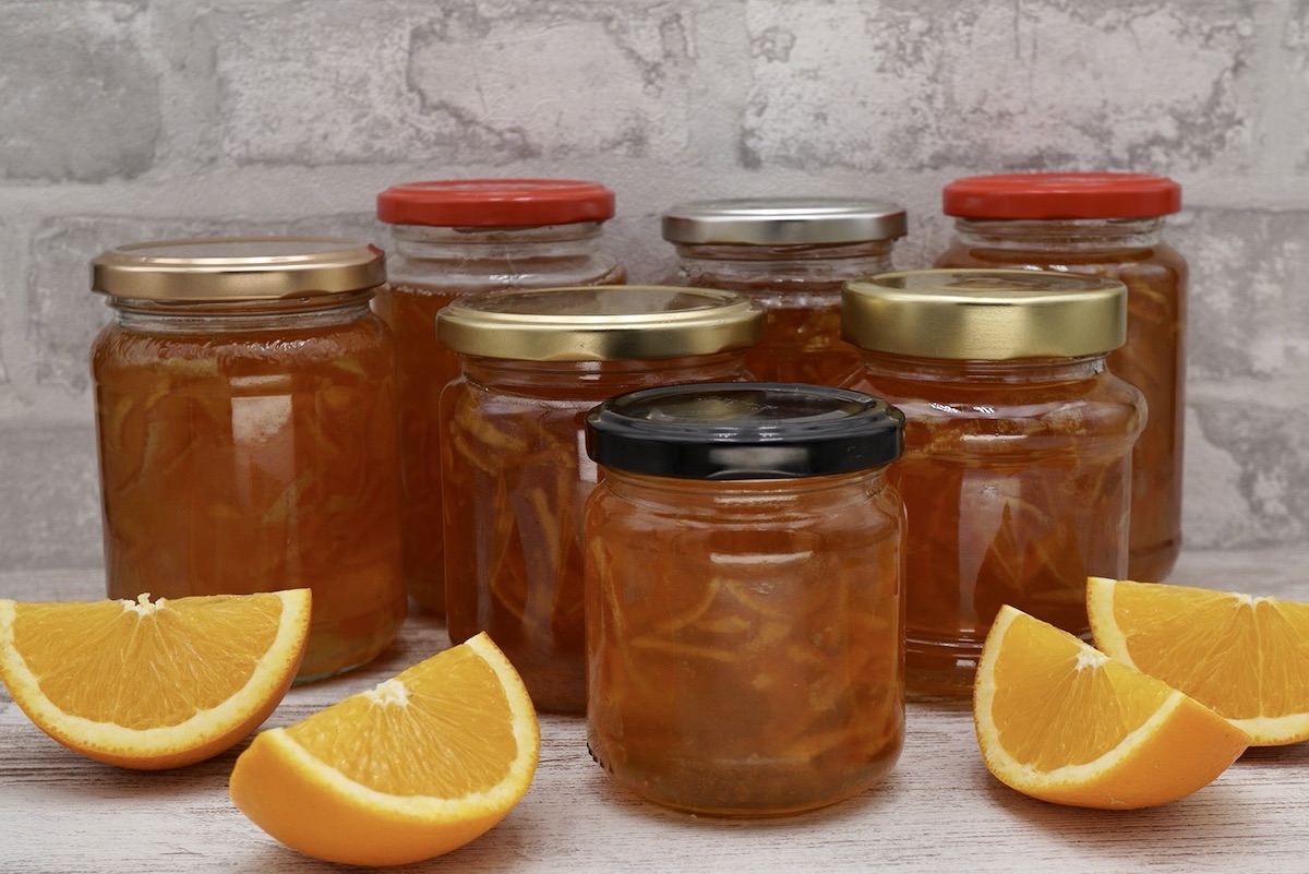 Several jars of homemade Seville orange marmalade and some segments of fresh orange.