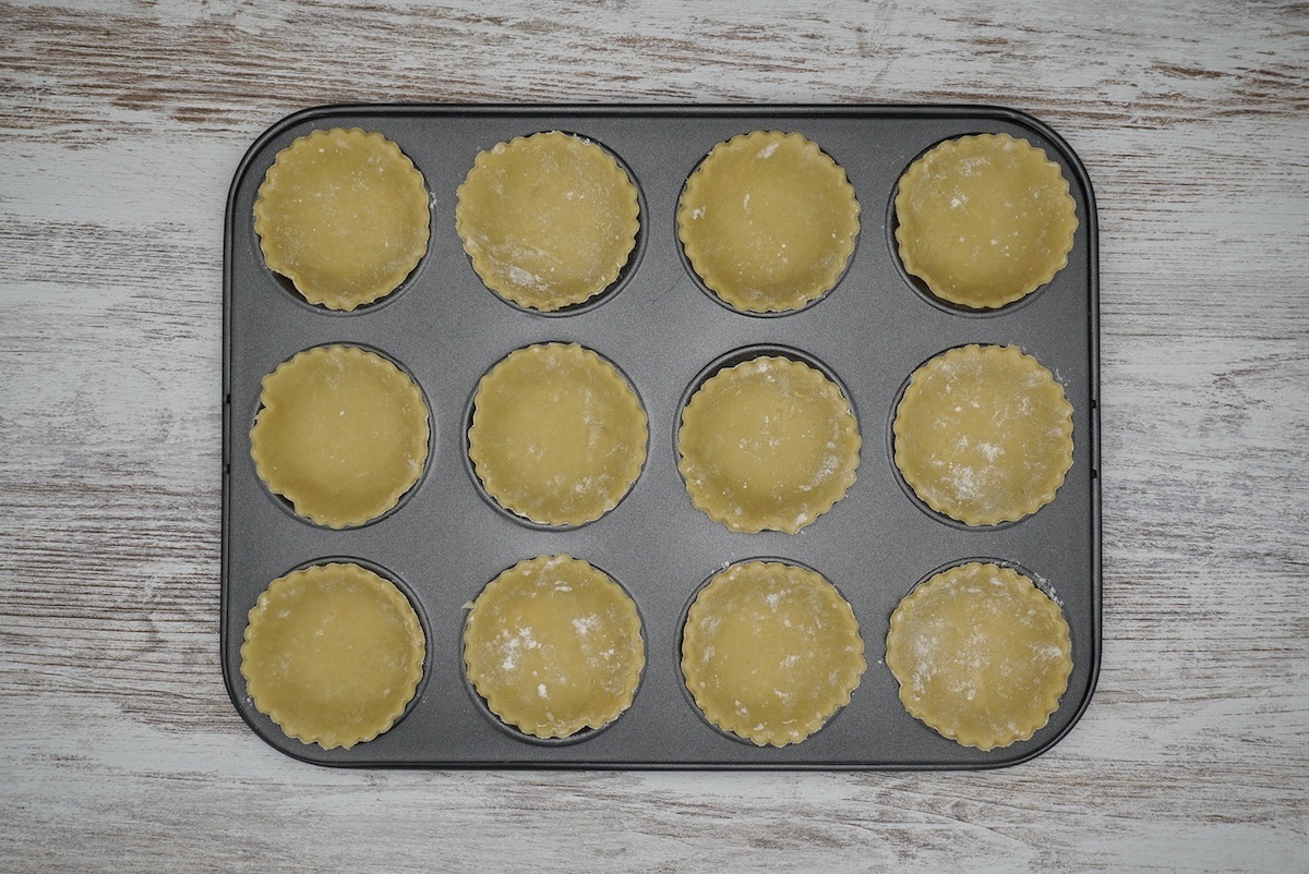 Twelve unbaked pastry cases in a tart tin.
