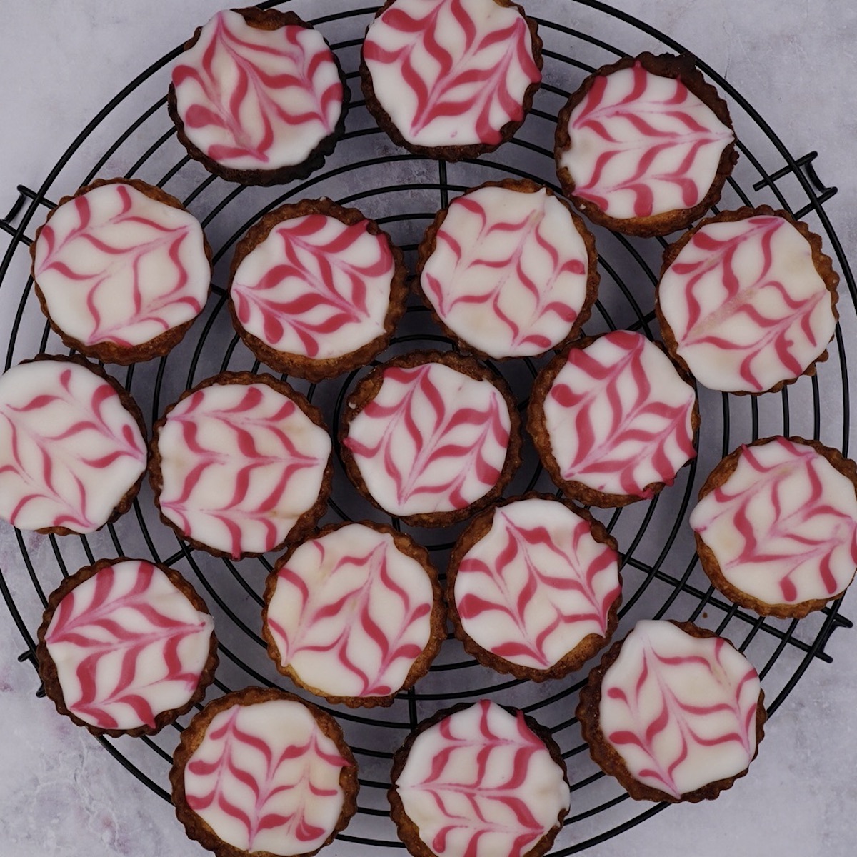 Several iced Bakewell tarts on a wire rack.