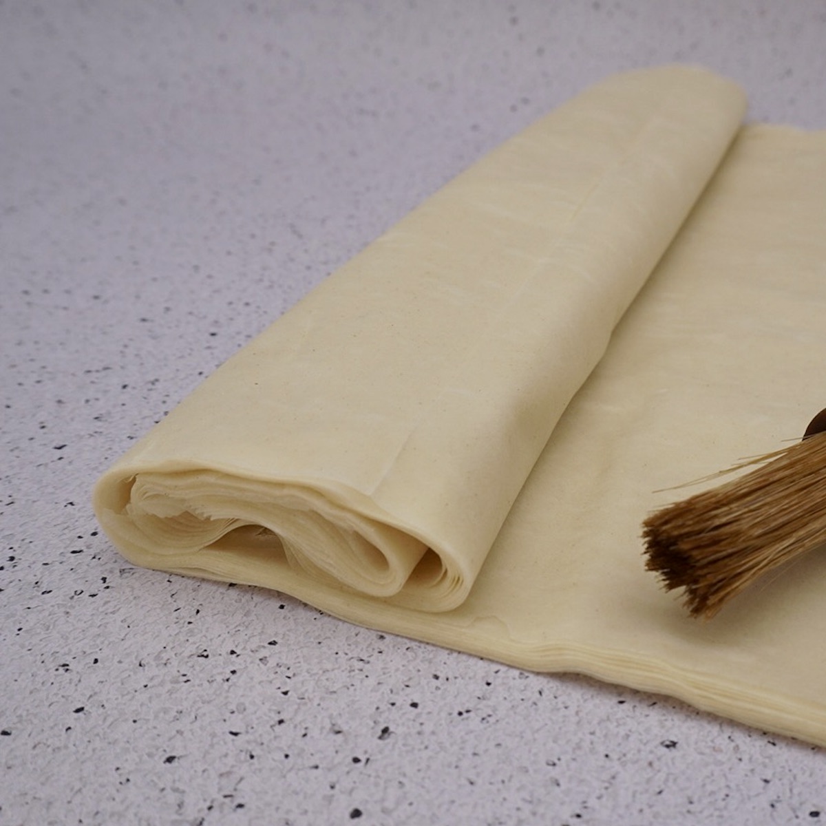 A roll of filo pastry on a speckled white kitchen worktop. 