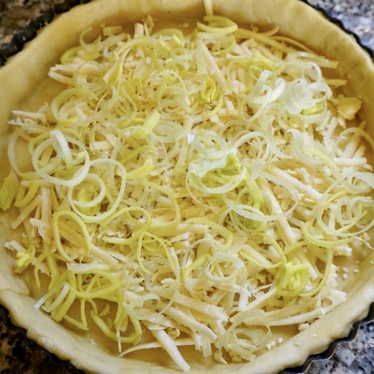 A pastry case with grated cheese and sliced leeks.