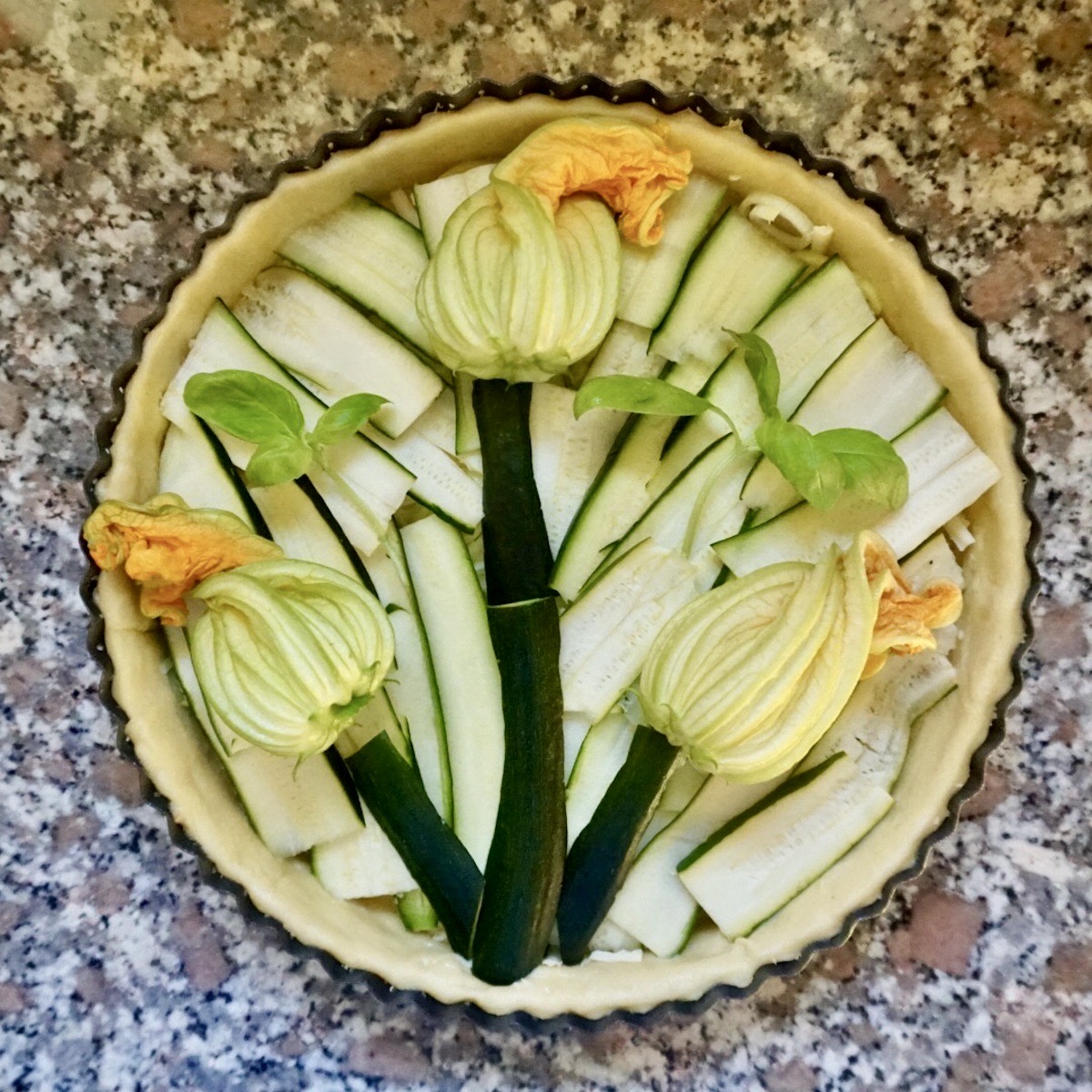 An uncooked courgette quiche decorated with courgette flowers.