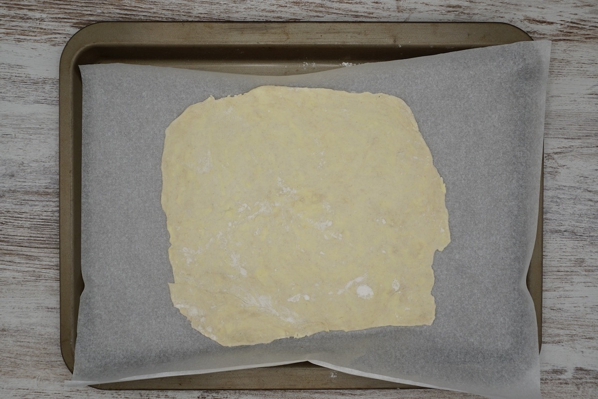 A rough square of uncooked pastry on a baking sheet.