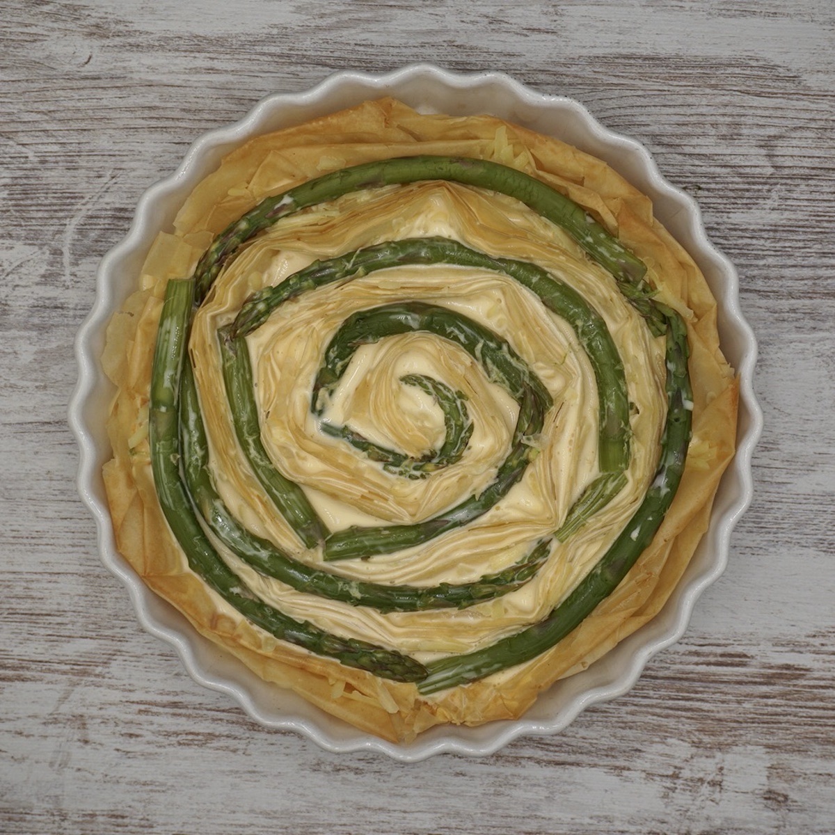 An unbaked filo quiche with asparagus formed in a spiral.
