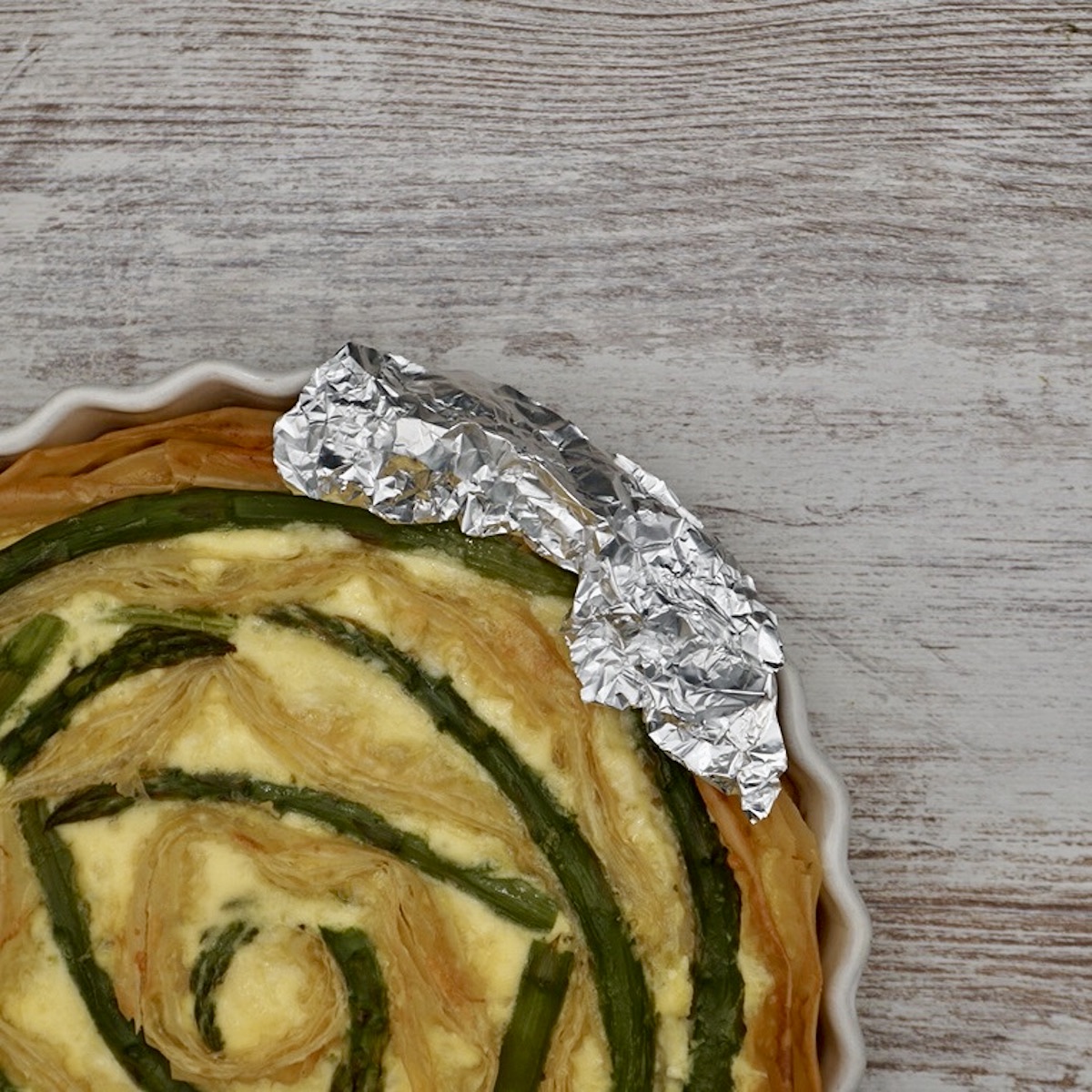 Part of a quiche with foil on part of the pastry.
