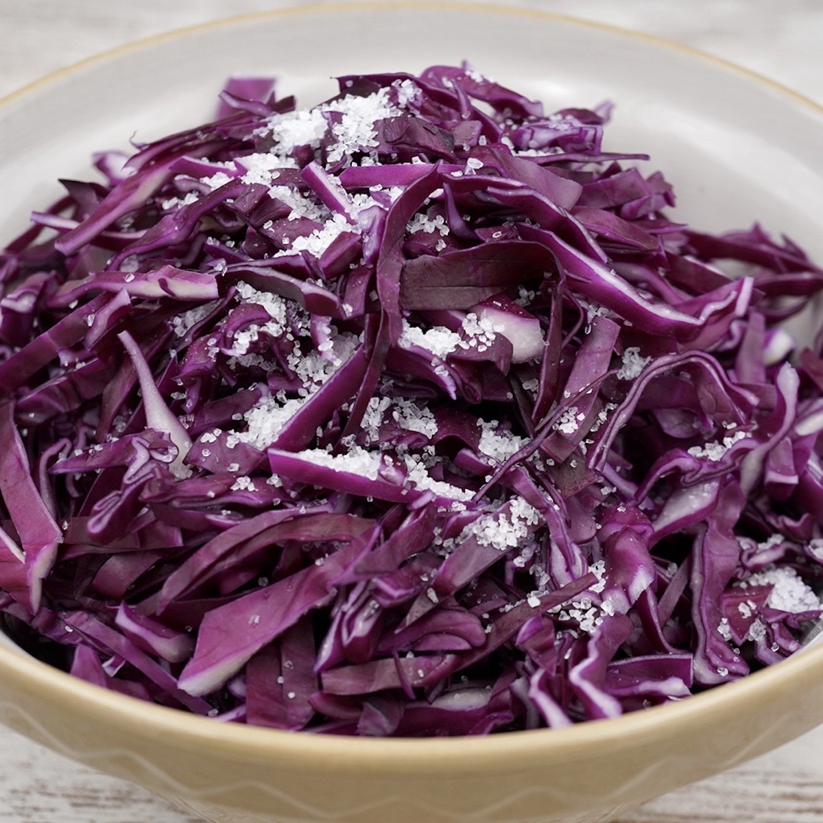 A bowl of shredded red cabbage with salt sprinkled on top.