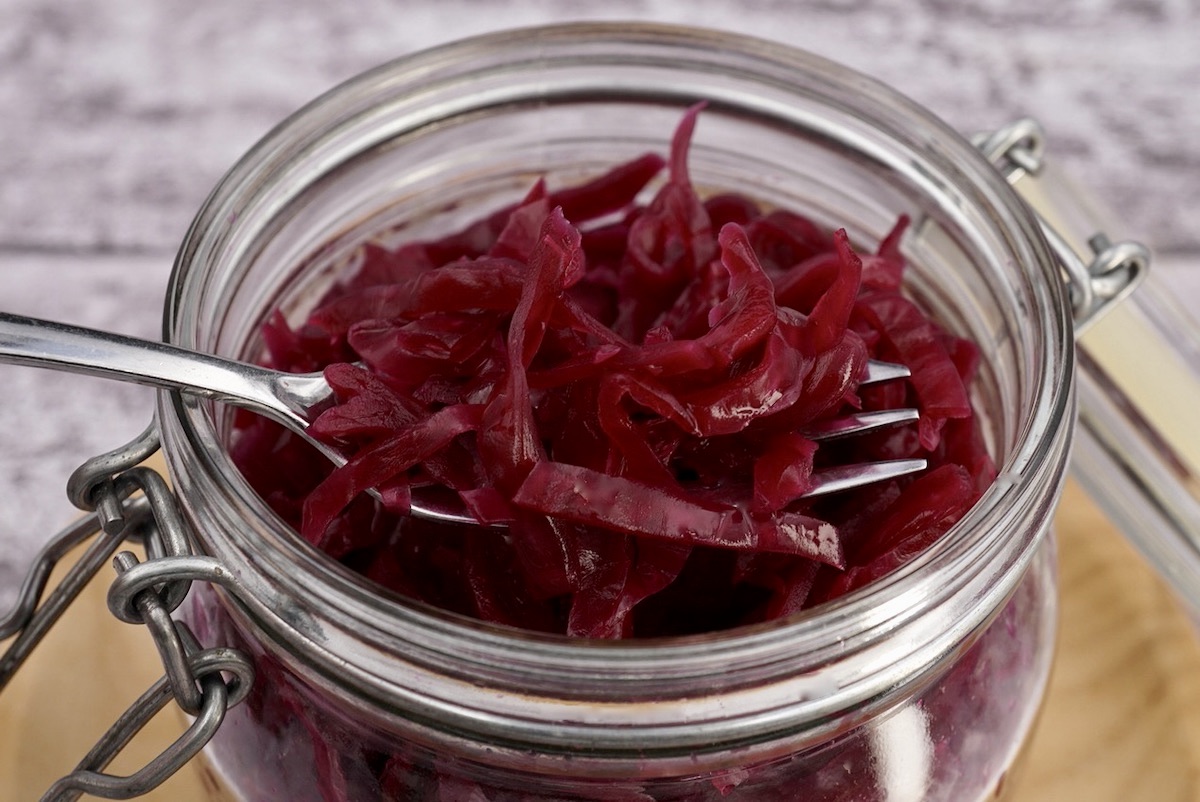 Red cabbage sauerkraut in a glass container with a fork.