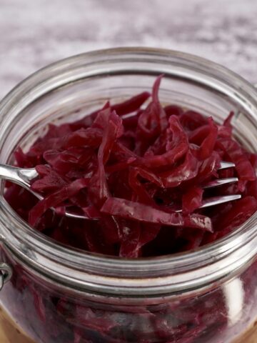Red cabbage sauerkraut in a glass container with a fork.