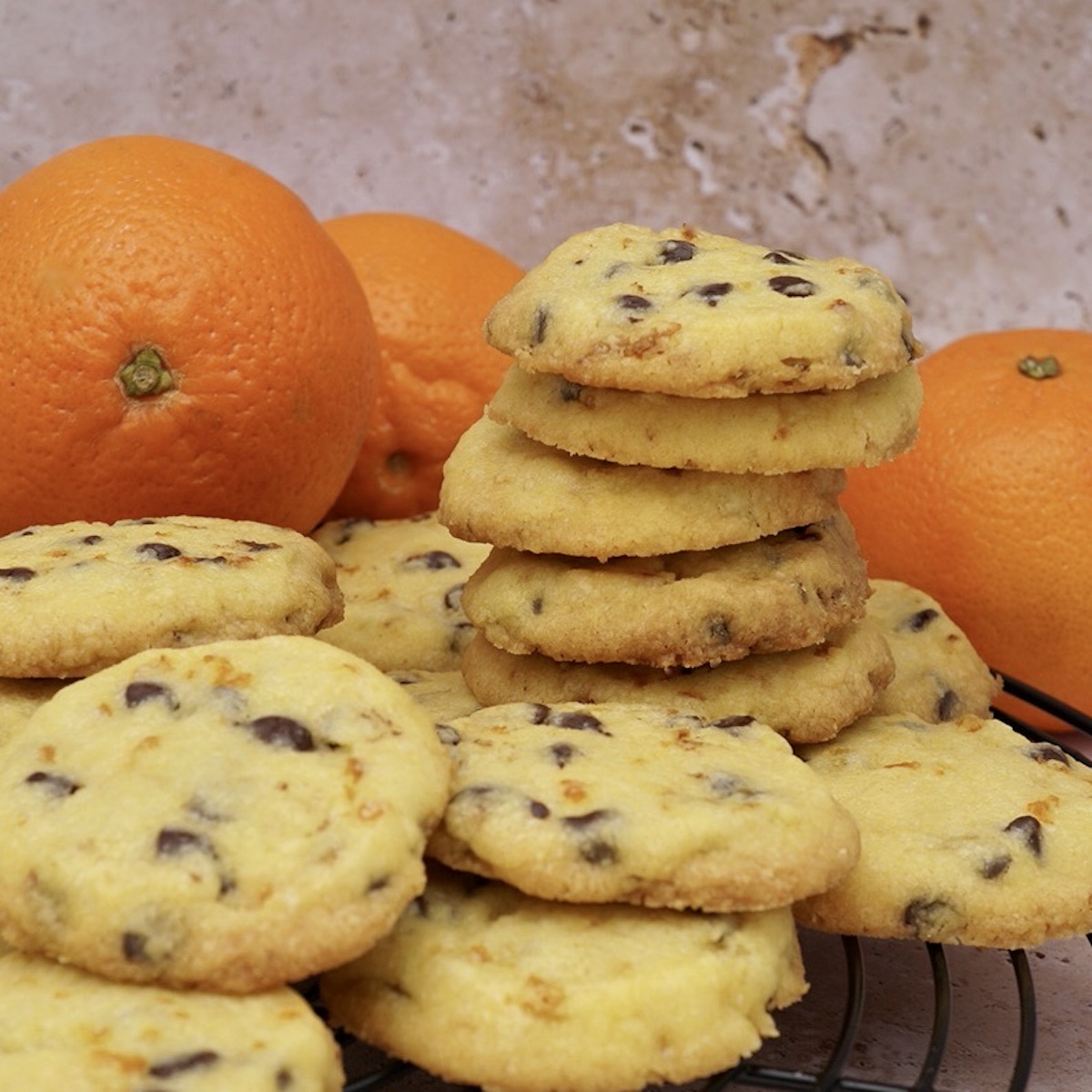 A stack of homemade chocolate orange shortbread biscuits with oranges behind.
