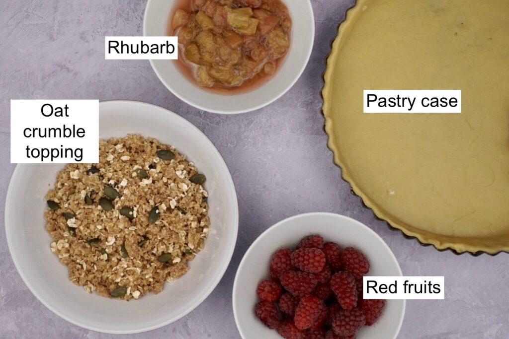A pastry case, a bowl of rhubarb, a bowl of red fruits and a bowl of crumble topping.