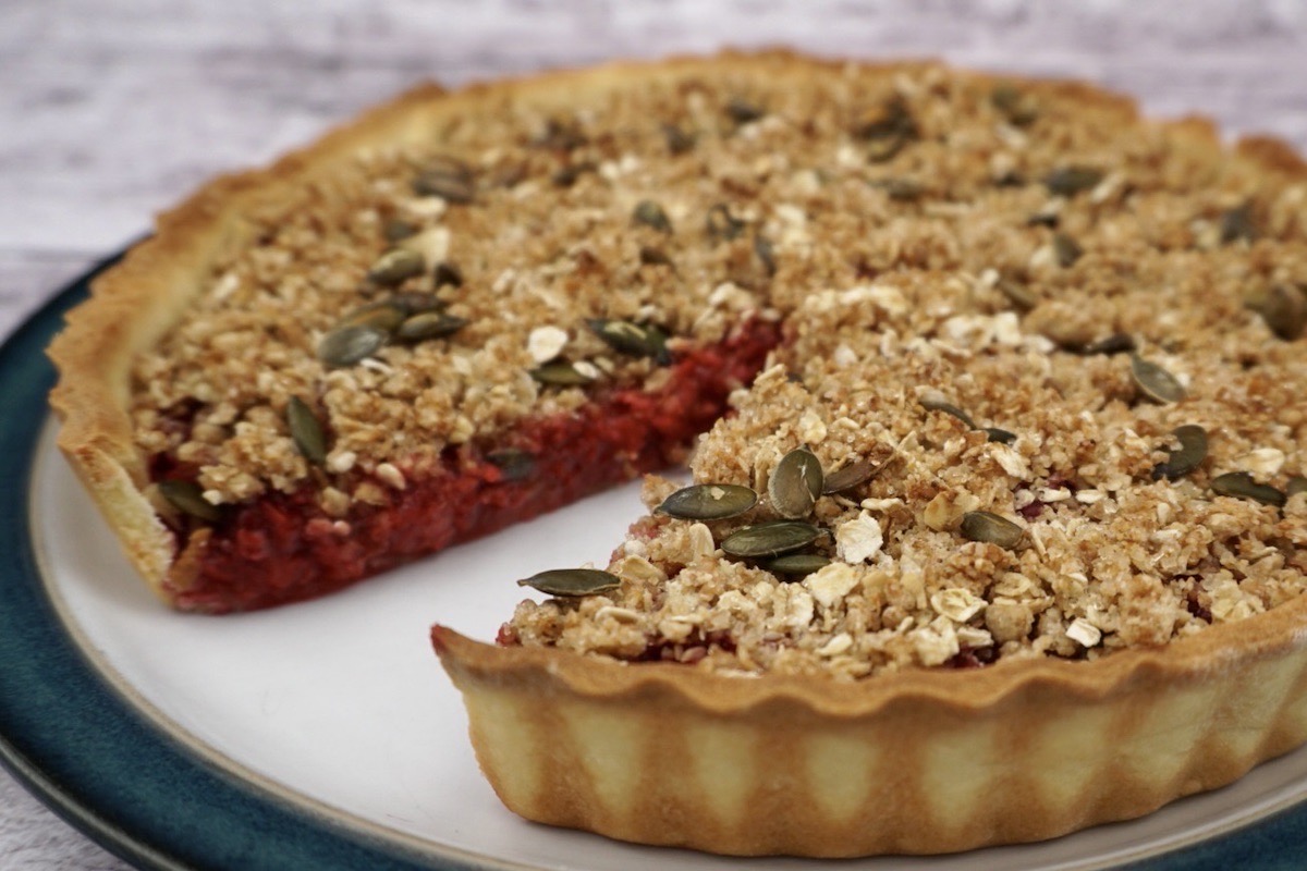 A fruit crumble tart with one slice missing. 