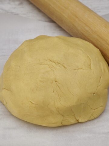 A ball of sweet almond shortcrust pastry next to a rolling pin.