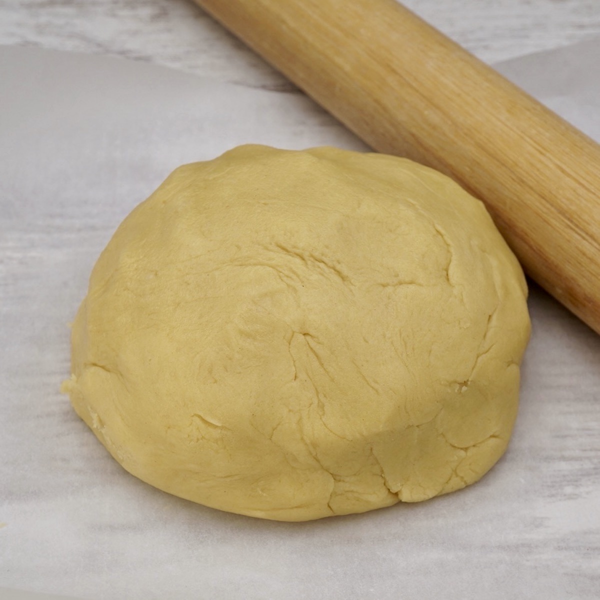 A ball of pastry dough next to a rolling pin. 