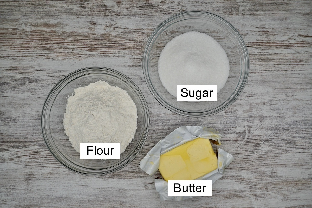 A bowl of sugar, a bowl of flour and a pack of butter with labels.