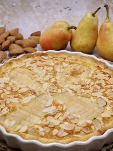 Pear and almond tart next to some pears and almonds.