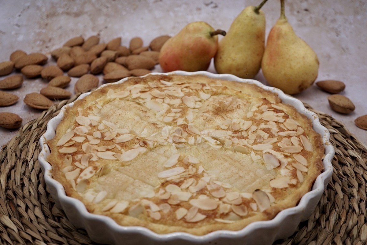 A pear and almond tart next to three pears and some almonds.