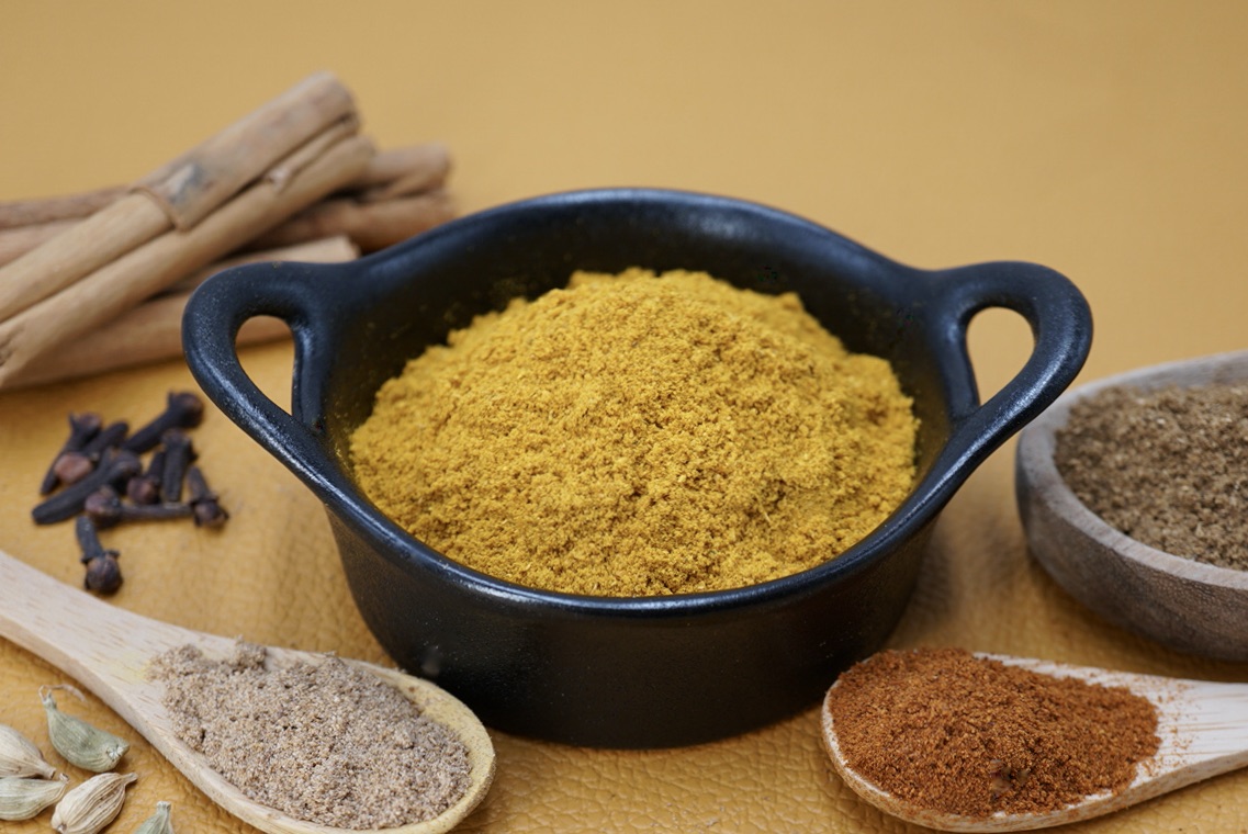 A bowl of curry powder next to some ground and whole spices.