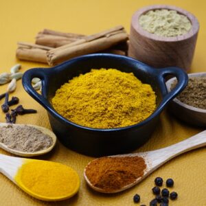 Curry powder in a bowl next to some ground and whole spices.