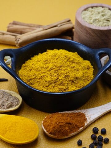 Curry powder in a bowl next to some ground and whole spices.