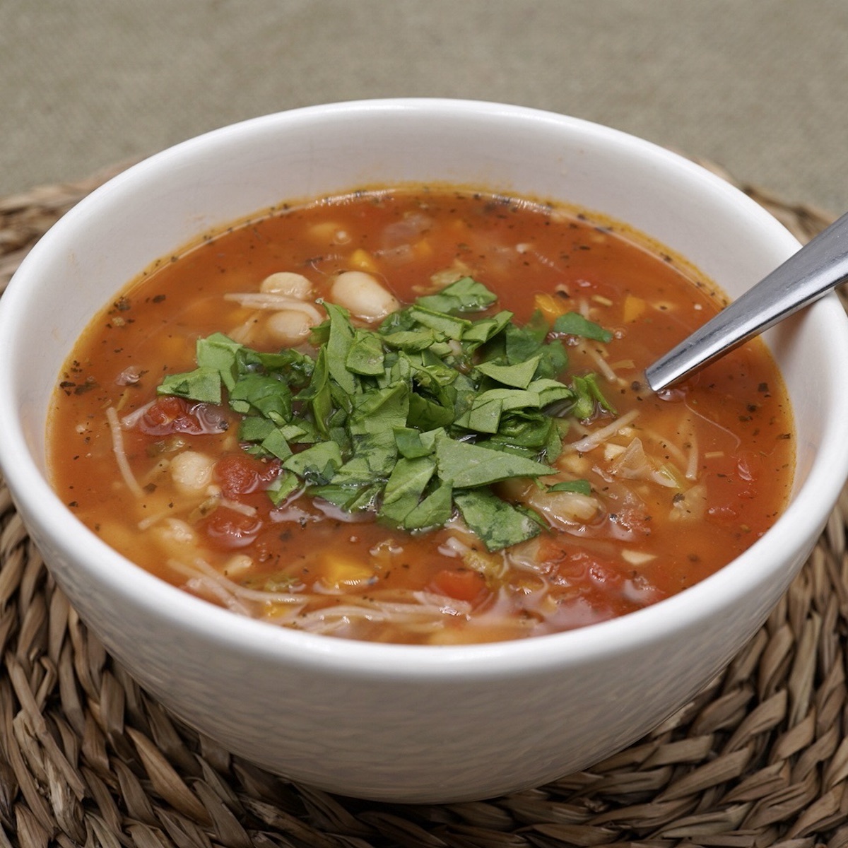 A bowl of tomato and bean soup with spinach garnish.