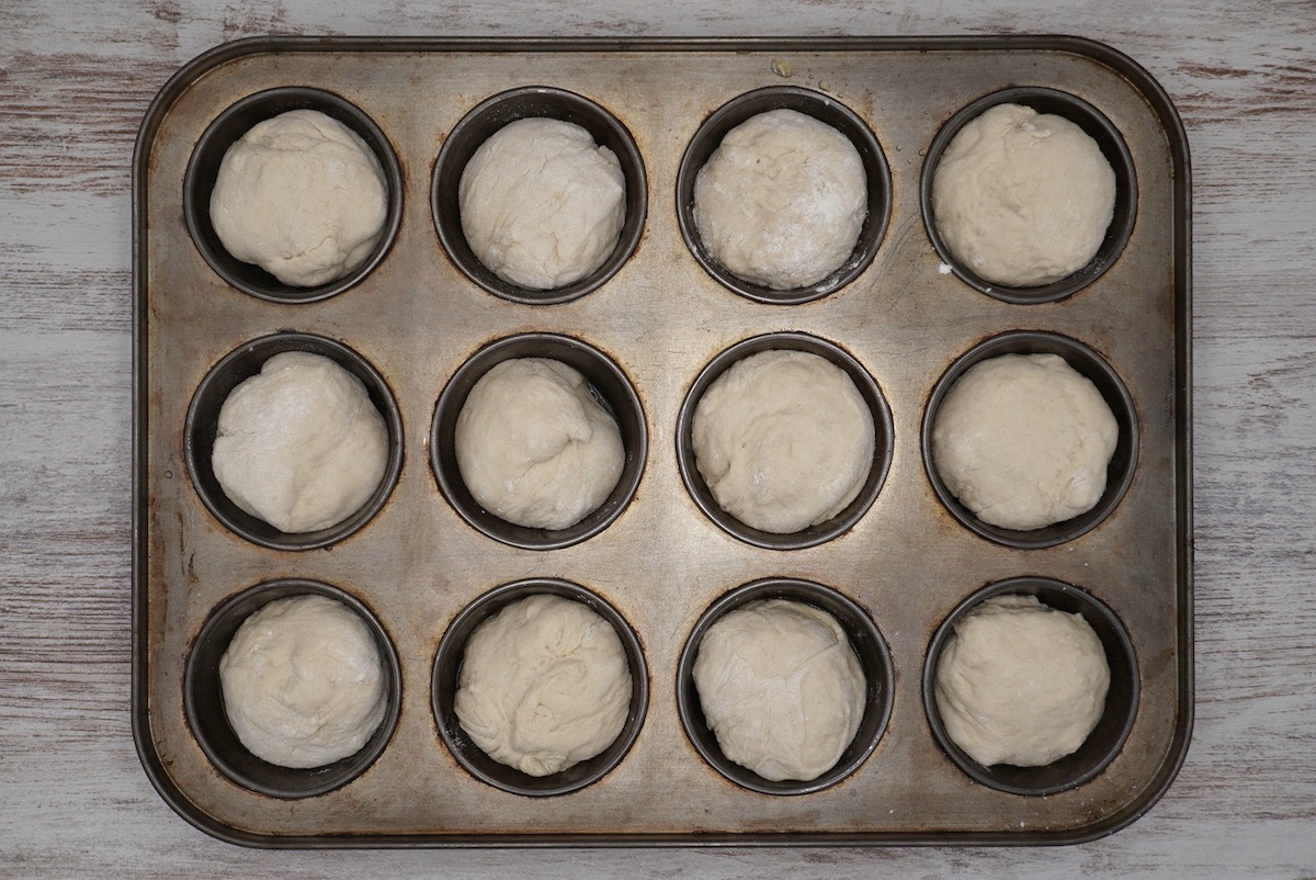 A twelve hole muffin tin with bread dough in each hole.