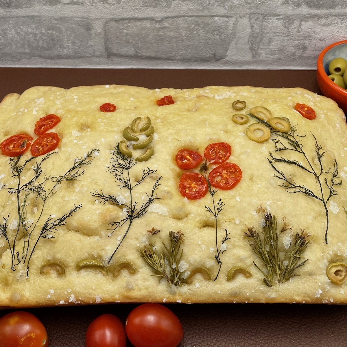 Homemade focaccia decorated with tomatoes, olives and herbs to form flowers. 