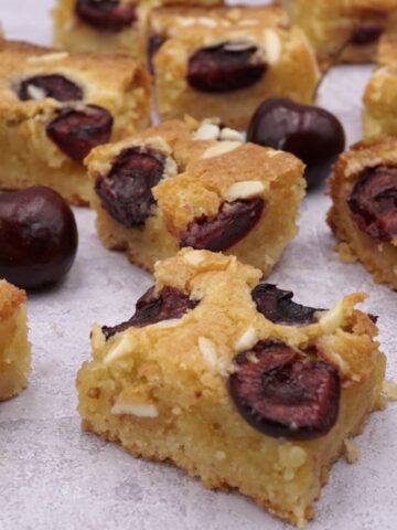 Several squares of cherry and almond traybake cake and some cherries.