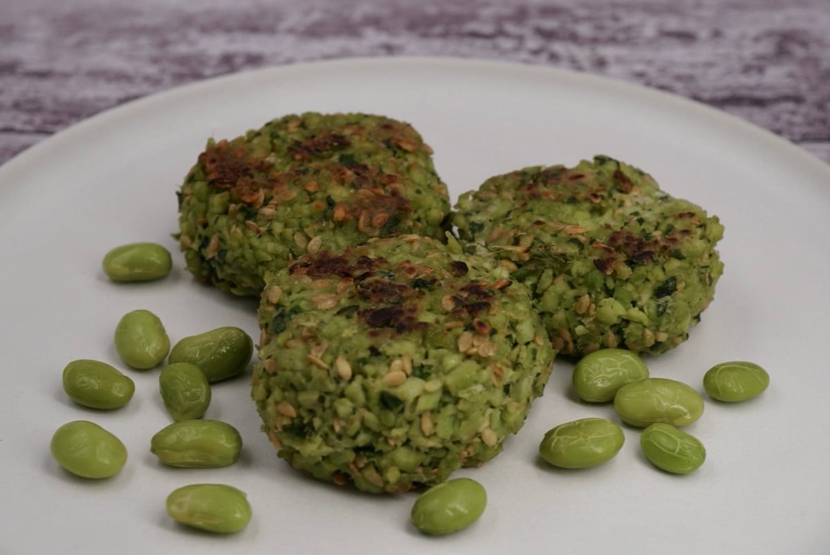 Three edamame bean fritters on a plate next to some beans.