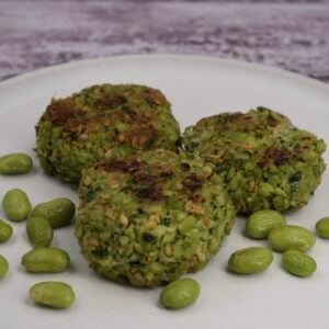 Three edamame bean fritters on a plate next to some beans.