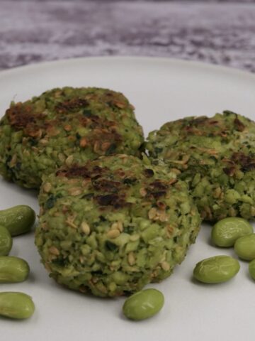 Three edamame bean fritters on a plate next to some beans.