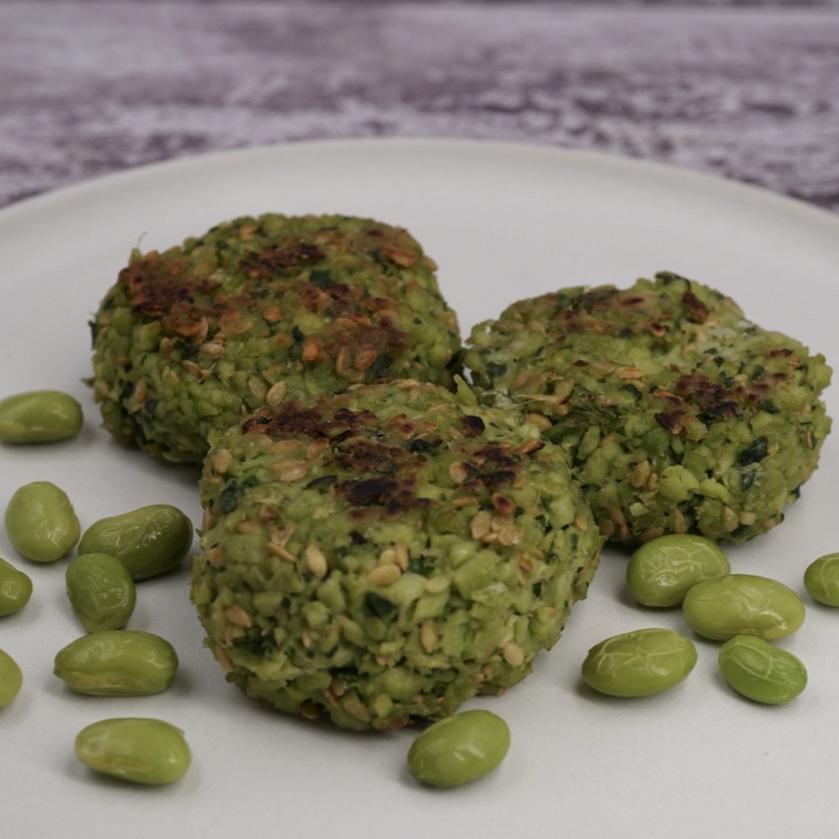 Three edamame fritters on a plate next to some beans. 