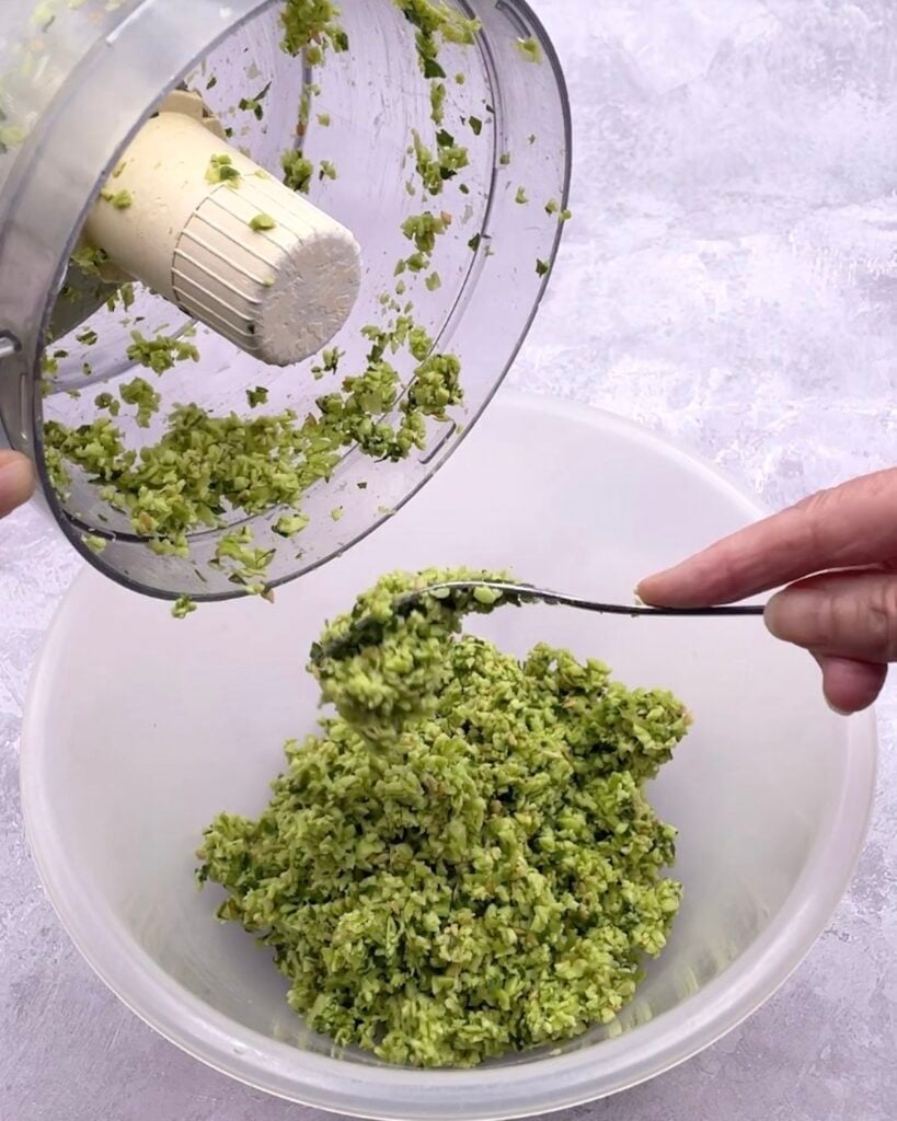 Chopped bean mixture being transferred from a food processor to a bowl.